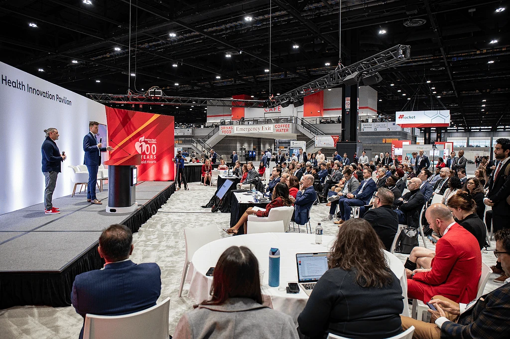 Two Powerful Medical presenters on stage at the AHA 2024 Health Innovation Pavilion before a seated audience